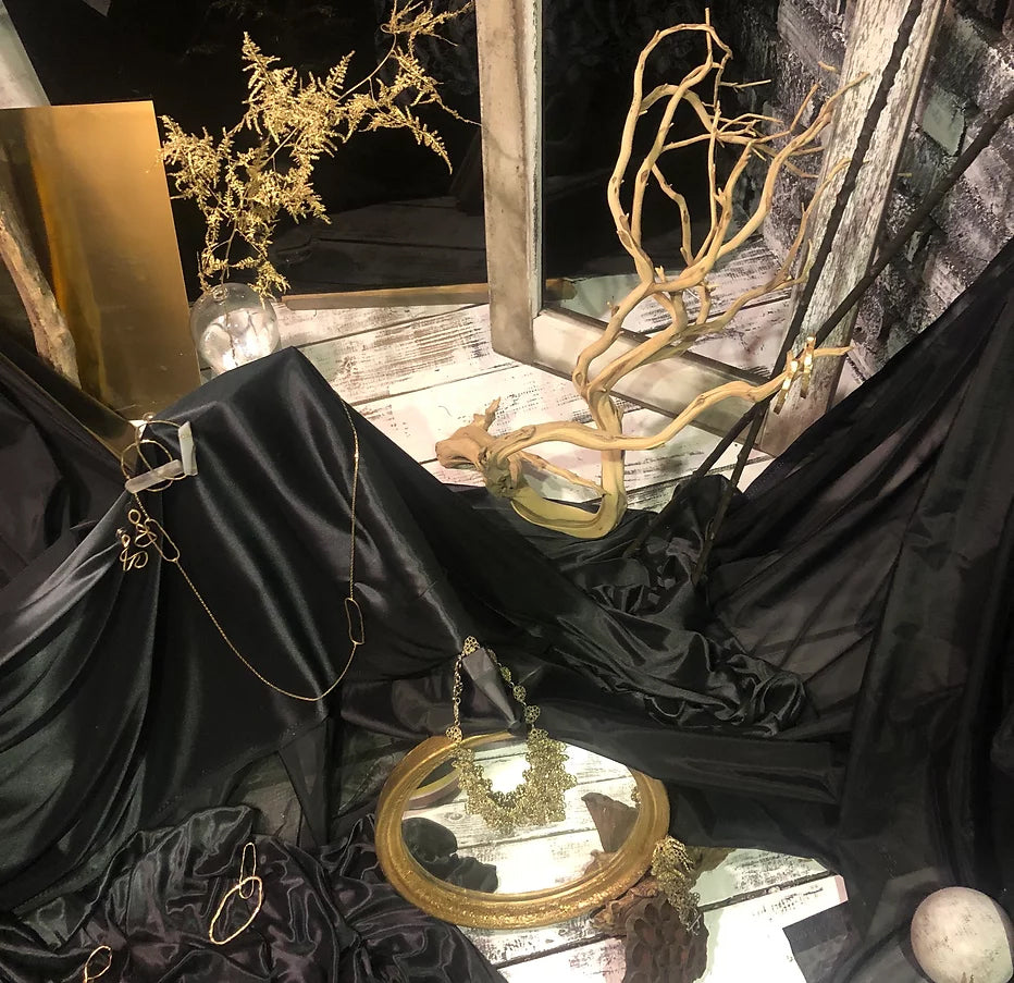 This image features an elegant jewelry display with a black silk background and dry plants